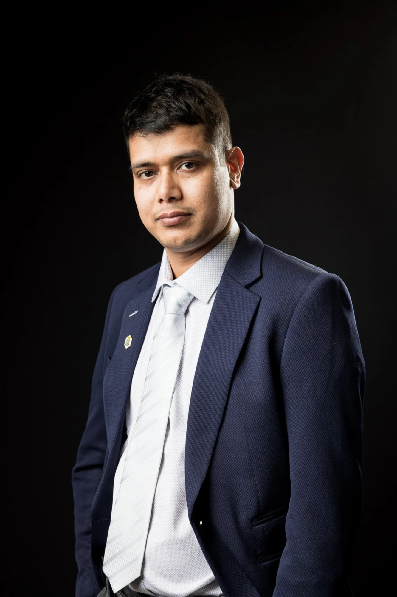 Khem Kadariya, founder of Living Rochester Suburbs, in a navy suit and silver tie against a black background