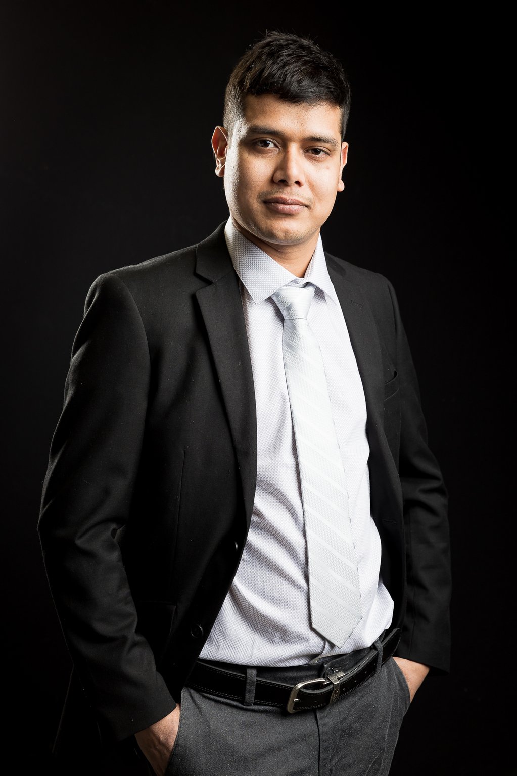 Khem Kadariya standing with hands in pockets against a dark background